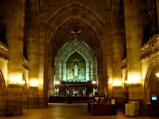 The interior of Sterling Memorial Memorial Library, with high vaulted ceilings the famous &quot;Alma Mater&quot; mural at the rear.
