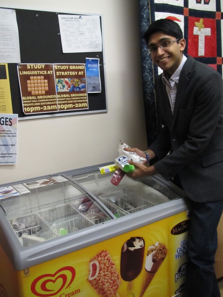 A student pulling an overflowing fistful of ice cream from the freezer.