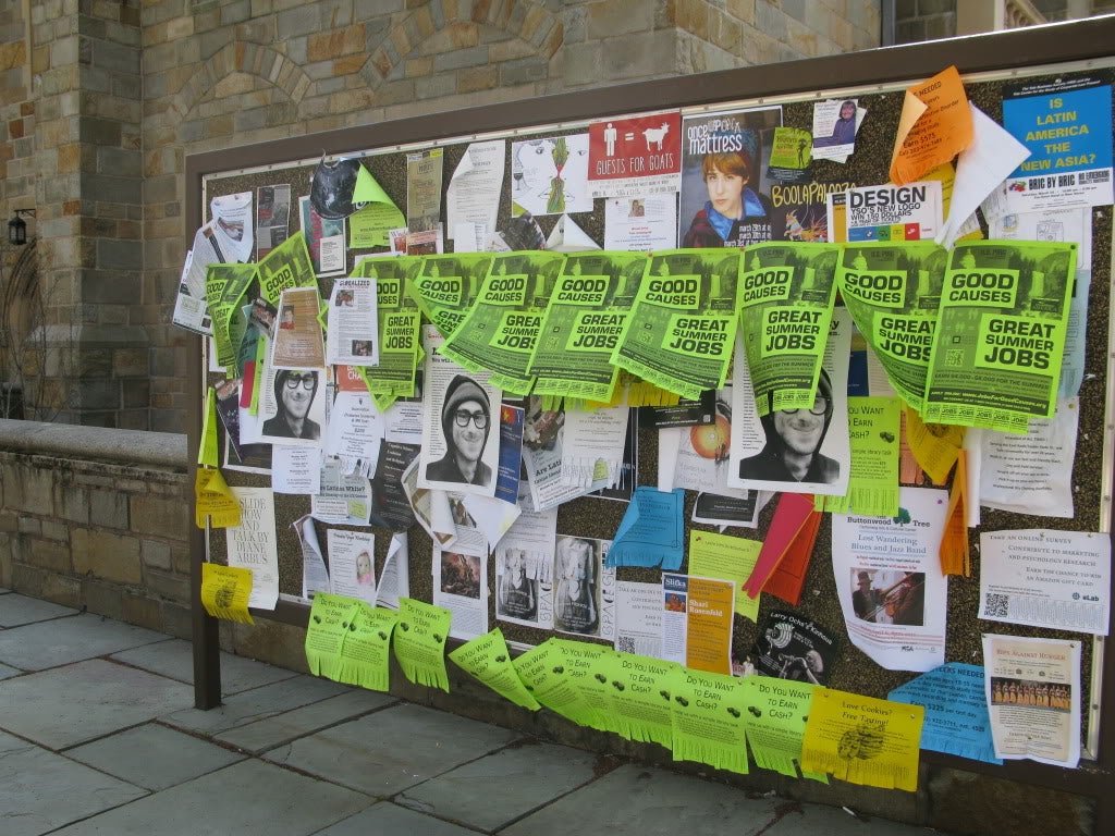 A campus bulletin board covered in fliers; several read &quot;Mitchell Dubey, you will never be forgotten&quot;
