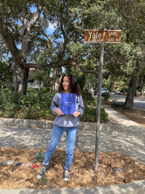 A girl standing on a street called Yale Avenue holding a Yale acceptance letter