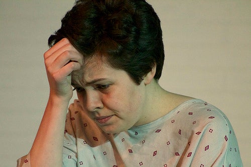 A distressed woman in a hospital gown, from a play.