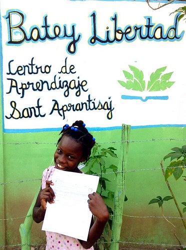 A young girl in front of literacy center, proudly holding up a book.