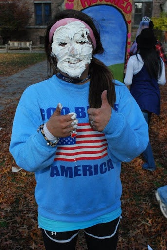 A girl gives two thumbs up, with her face covered in whipped cream.