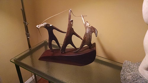 An Eskiimo wood carving of three men on a boat holding a rope.