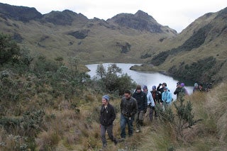 The student group walking through a grassy mountain valley by a lake.