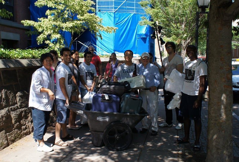Lamtharn on move-in day with a wheelbarrow full of luggage, accompanied by move-in staff and OISS counselors.