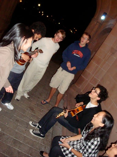 Students singing and playing string instruments under the archway.