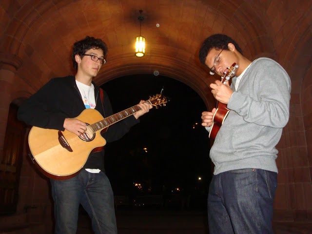Two male students playing guitar and ukulele underneath the Vanderbilt arch.