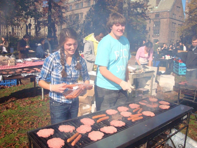Two FCC members putting burgers and hot dogs on the grill.
