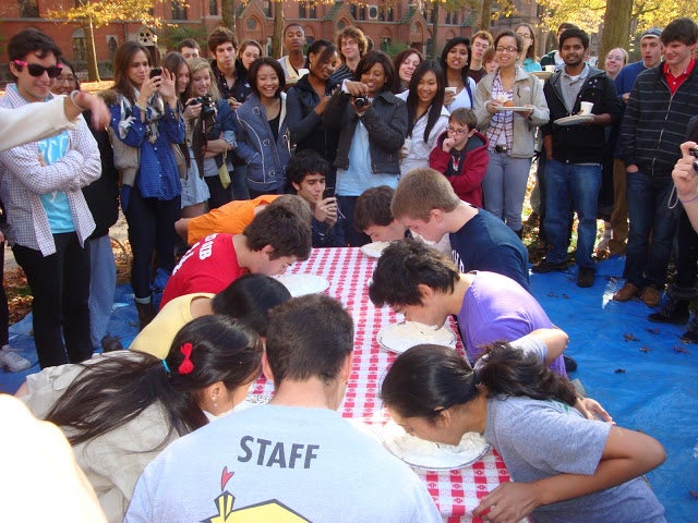 Students at a picnic table burying their faces into cream pies.