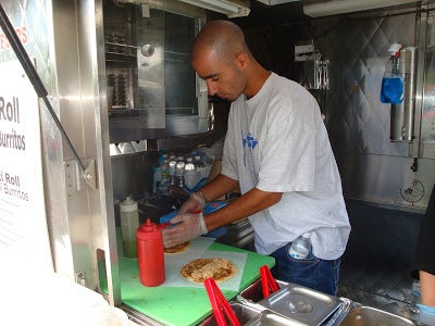 A cook assembling a Kati roll, placing ground chicken on pita bread.