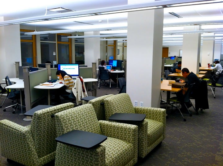 Comfortable armchairs with surfaces for laptop computers. Nearby, individual workstations and long tables.