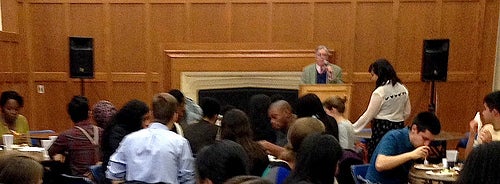 A faculty member speaking at the podium as students eat at the tables.