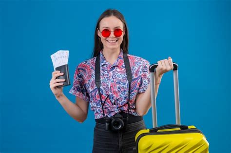 Woman holding passport and luggage in front of blue wall
