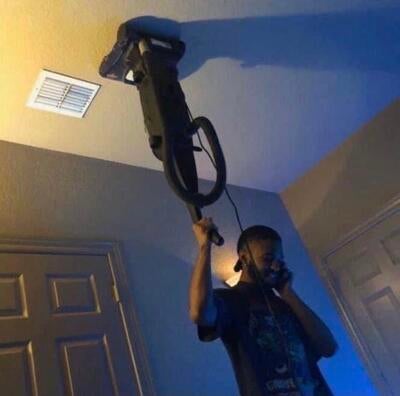 A man on the phone, absentmindedly vacuuming his ceiling.