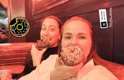 two girls smile holding donuts in front of their mouths
