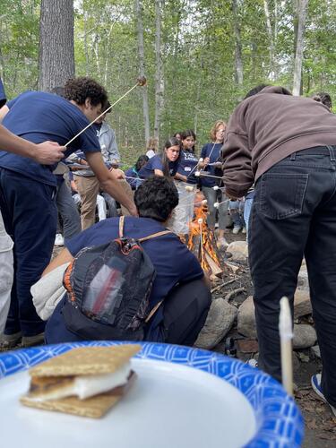A group of students from La Casa toasting marshmallows in a forest setting.