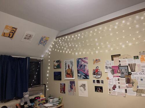 Yale dorm bedroom wall decorated with various posters, a collage, and fairy lights
