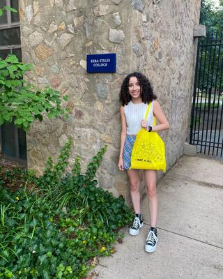 A smiling girl standing in front a sign that says Ezra Stiles College