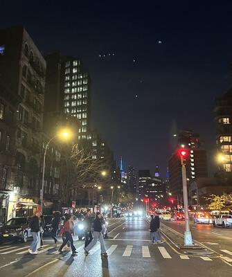 Busy NYC street at night, Empire State Building illuminated blue in the far distance