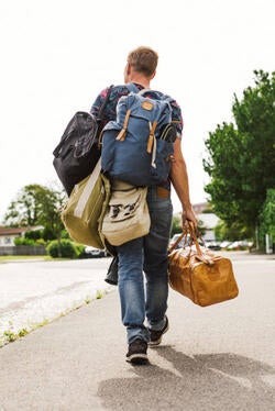 Man carrying luggage and bags and walking away from camera