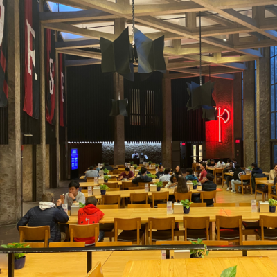 Morse College dining hall with light wooden tables, red ax sign on wall, and students eating. 