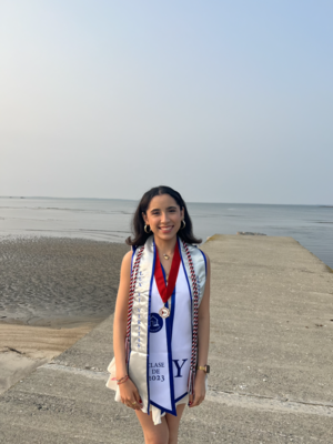 A young woman standing in front of an ocean proudly showing her graduation stoles