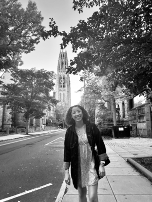 A black and white photo of a girl smiling in front of a bell tower