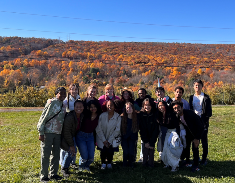 Students gathering as a group in front of fall leaves