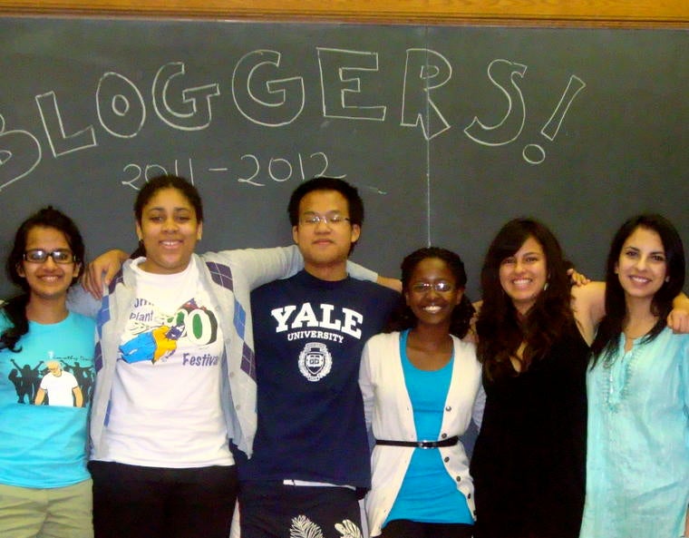 A diverse group of students standing in front of a blackboard reading "Bloggers! 2011-2012".