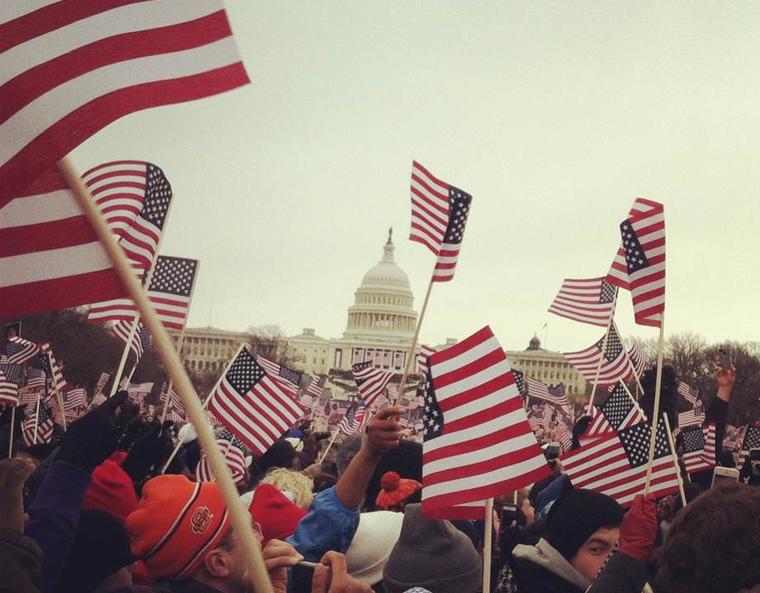 A dense crowd of people waving small American Flags in front of the United States Capital Building.