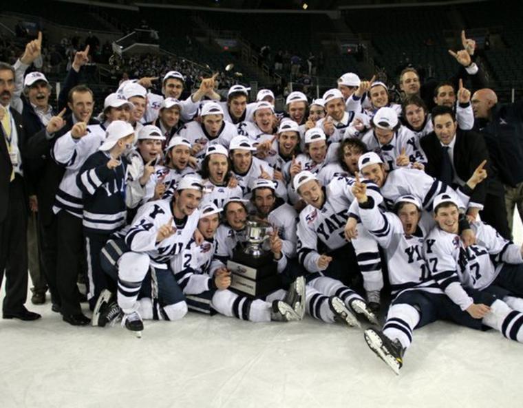 The Yale Men's Hockey team in celebration, holding a gold trophy.