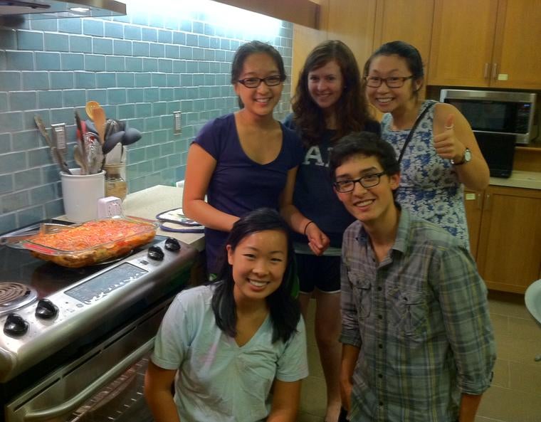 A group of students pose with a freshly-cooked dinner in a residential college kitchen.