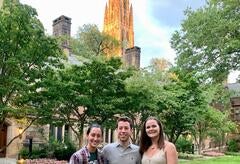 three people stand in the courtyard in front of an illuminated Harkness Tower