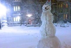 A tall snowman standing outside a residential college.